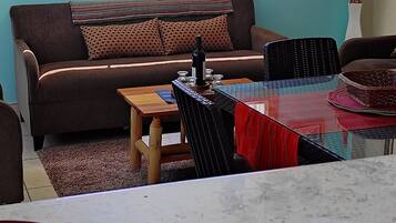 Sala de estar com sofá, mesa de jantar e vista para montanhas através de uma grande janela.