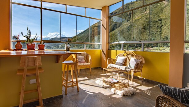 Una habitación luminosa con ventanas amplias, una barra de madera, muebles de mimbre y vistas a la montaña.