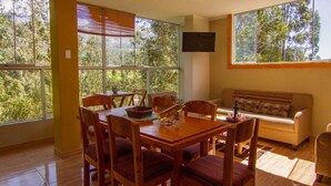 Un comedor con mesa y sillas de madera, un sofá y ventanas amplias con vistas a árboles.