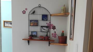 A corner room with a wooden desk, a chair, a wall-mounted shelf with potted plants, and a birdcage decoration.
