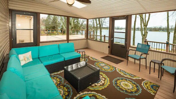 A covered outdoor deck with a turquoise sofa, a small table, and chairs. - The Sanctuary on Golden Lake (Pleasant Lake)