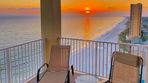 Un balcone con due sedie, vista sul tramonto sull'oceano e un edificio sullo sfondo.