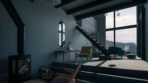 Ein modernes Wohnzimmer mit Kamin, gemütlicher Sitzecke, einer Treppe, die zu einem Balkon führt, und großen Fenstern mit Aussicht.