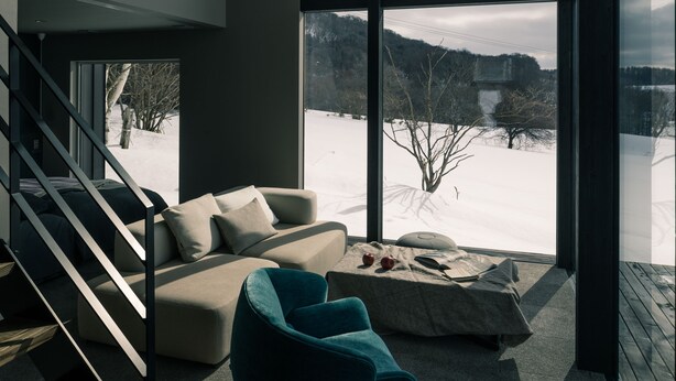 Ein modernes Interieur mit einem großen Fenster, einem Sofa, einem Sessel und einer Treppe.