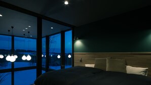 Ein modernes Schlafzimmer mit einem großen Bett, einem Holzkopfende und Blick auf eine verschneite Landschaft durch raumhohe Fenster.