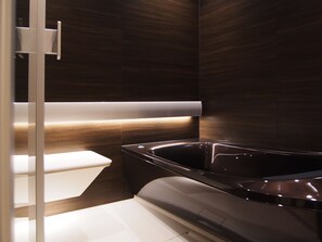 Un baño moderno con una bañera negra, inodoro blanco y cabina de ducha con mampara de vidrio.
