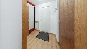 A hallway with wooden flooring, a black doormat, and a white door with a red trim. - Homerez - Studio in Gérardmer (Gérardmer)