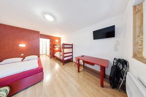 Una stanza con un letto a castello, una scrivania, una sedia, un televisore e un termosifone.