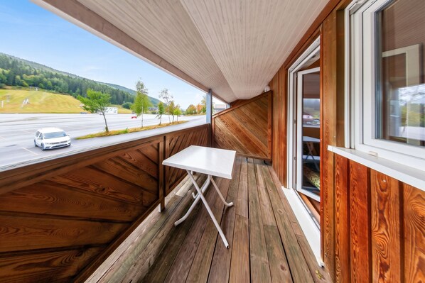 A wooden deck with a table and a window overlooking a road and trees.