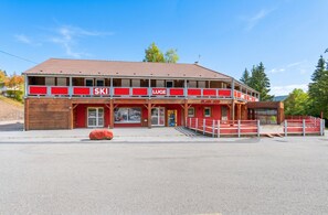 Un edificio a due piani con un cartello per sci e slittino, una facciata in legno e una panca rossa all'esterno.