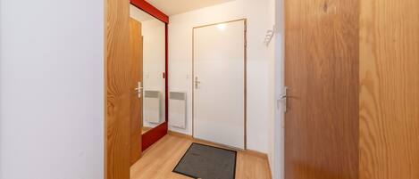 A hallway with wooden flooring, a red-framed mirror, a white door, and a white radiator.