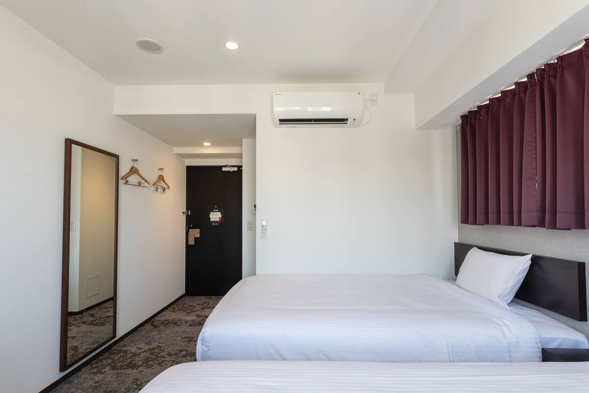 A hotel room with two beds, a mirror, a door, and an air conditioning unit.