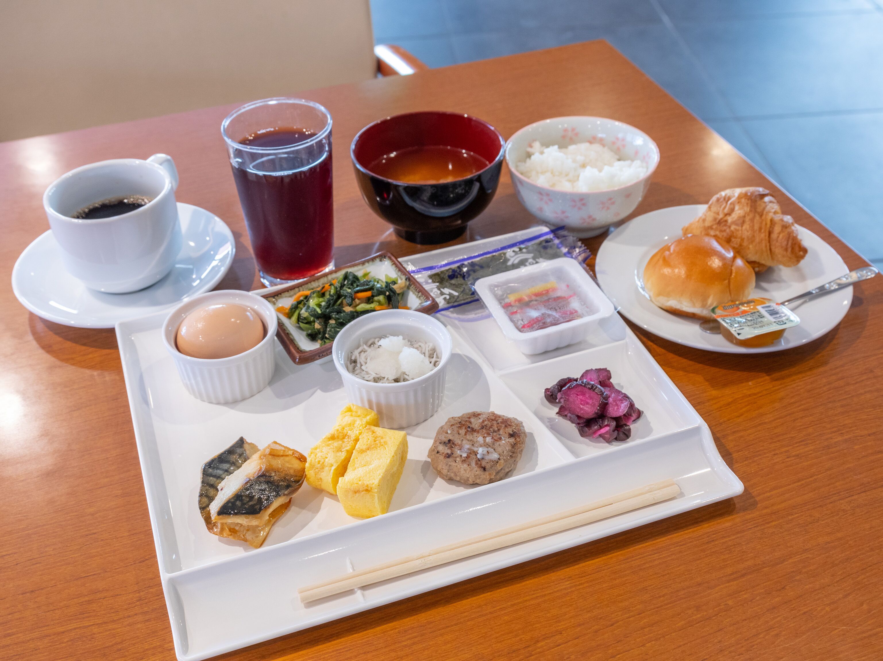 Una bandeja con diversos platos japoneses, como sushi, arroz y un croissant.