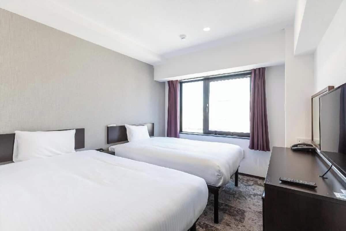 A hotel room with two beds, a desk, a TV, and a window with curtains.
