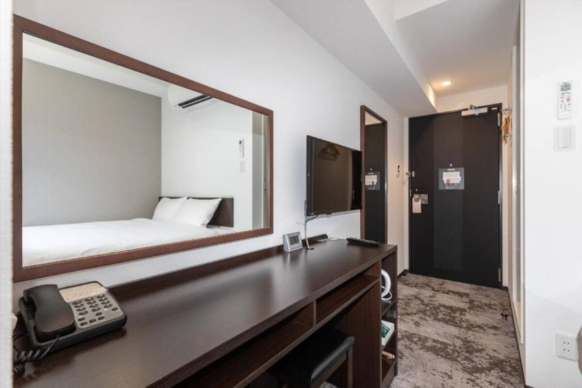 A hotel room with a bed, a desk with a phone, a TV, and a door.