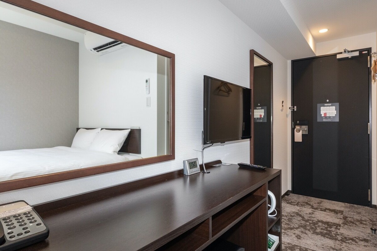 Een hotelkamer met een bed, een grote spiegel, een televisie, een bureau met telefoon en een deur naar de badkamer.