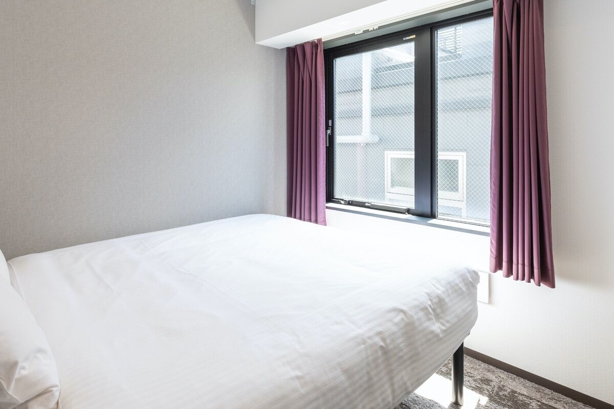 Een eenpersoonsbed in een kamer met een raam en gordijnen.