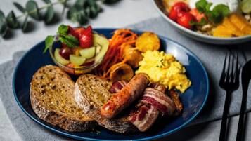 Ein Frühstücksteller mit Toast, Würstchen, Rührei und einem kleinen Salat.