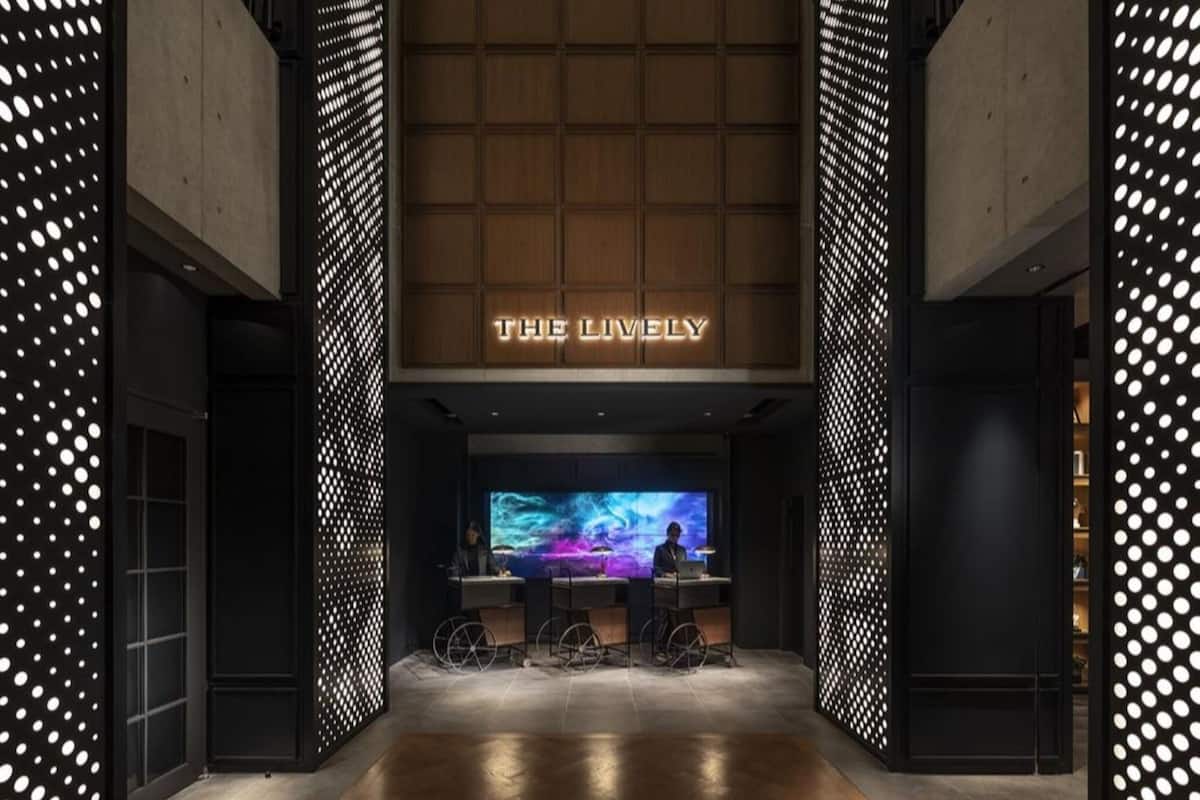 A modern hotel lobby with a large digital screen displaying a scenic image, a reception desk, and a bar area with stools.