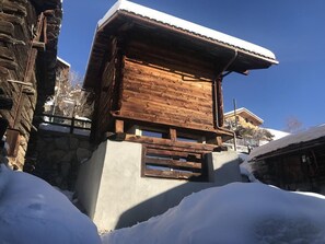 A wooden chalet with a stone base, surrounded by snow, under a clear blue sky. - ATTIC VALAISAN TYPICAL (Mase)