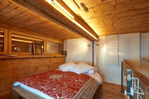 A wooden room with a bed, a window with blinds, and a shelf with items. - ATTIC VALAISAN TYPICAL (Mase)