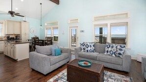 A spacious living area with two grey sofas, a dining table, and a kitchen in the background.