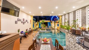 Un área de recepción con piscina, mostrador de madera, sillas y una mesa de comedor con frutera.