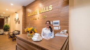 Un mostrador de recepción con detalles de madera, un letrero que dice "Golden Walls" y un jarrón con girasoles.