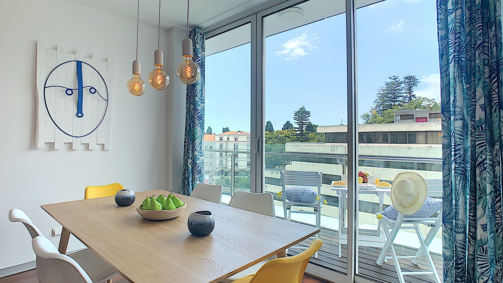 A modern dining area with a wooden table, chairs, and a view of the city through large windows.