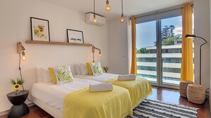 A modern bedroom with a large bed, two bedside tables, a floor lamp, and a view of the city through a sliding glass door. - Apartment Sunniva by LovelyStay (Funchal)