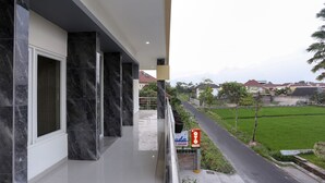 A modern building with a balcony overlooking a green field and a road. - OYO 999 Garuda Guesthouse (Ngaglik)