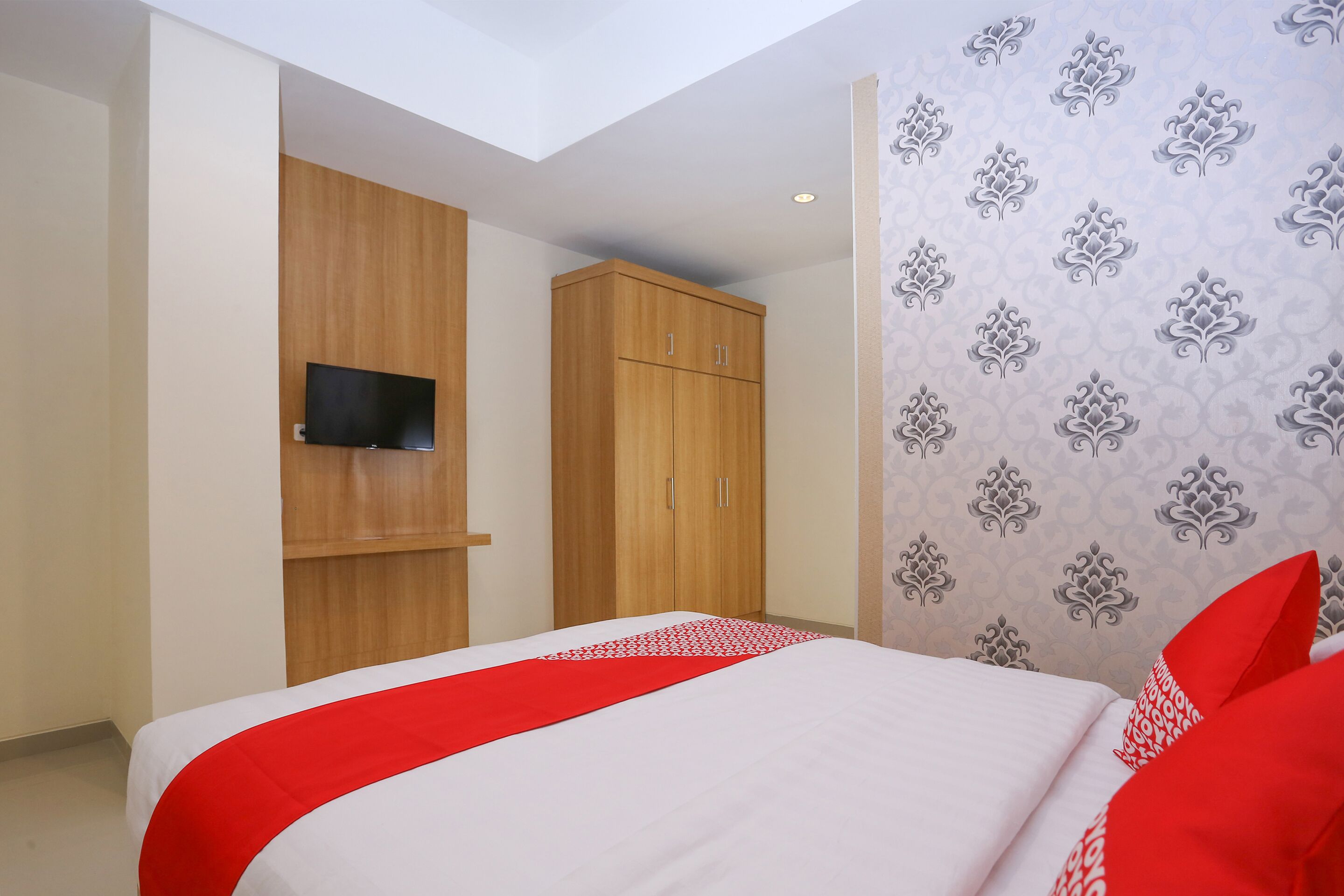 Una habitación de hotel con una cama, un televisor montado en la pared, armarios de madera y un papel tapiz estampado.