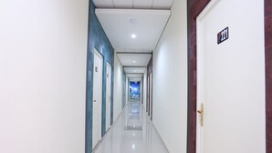 A long, narrow hallway with doors on both sides, a white ceiling with recessed lighting, and a blue wall on the left. - OYO 999 Garuda Guesthouse (Ngaglik)