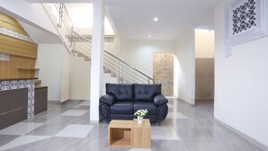 A modern living room with a black leather sofa, a wooden coffee table, and a staircase leading to an upper floor. - OYO 999 Garuda Guesthouse (Ngaglik)
