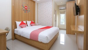 A hotel room with a wooden bed, white bedding, red and white pillows, a mounted TV, and a wooden wardrobe. - OYO 999 Garuda Guesthouse (Ngaglik)
