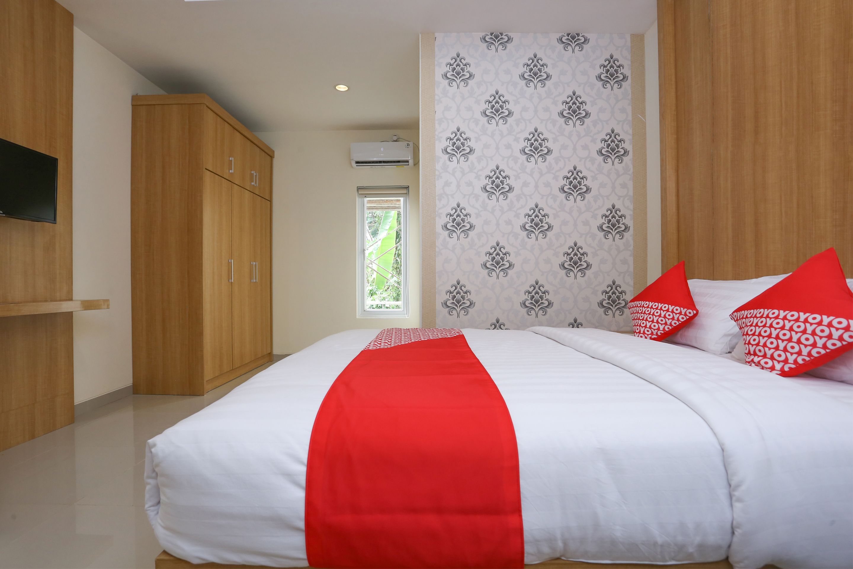 A bedroom with a bed, wooden wardrobe, and a wall-mounted TV.