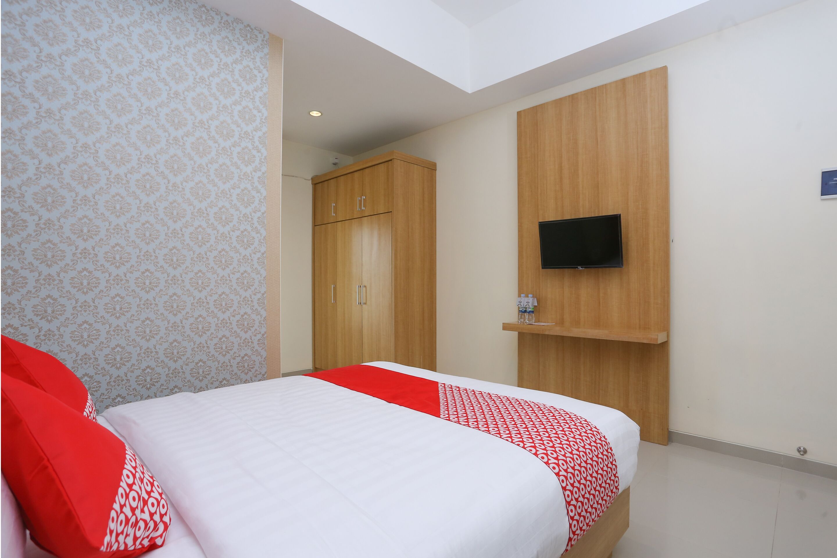 A hotel room with a bed, a wardrobe, a TV, and a shelf with bottles.