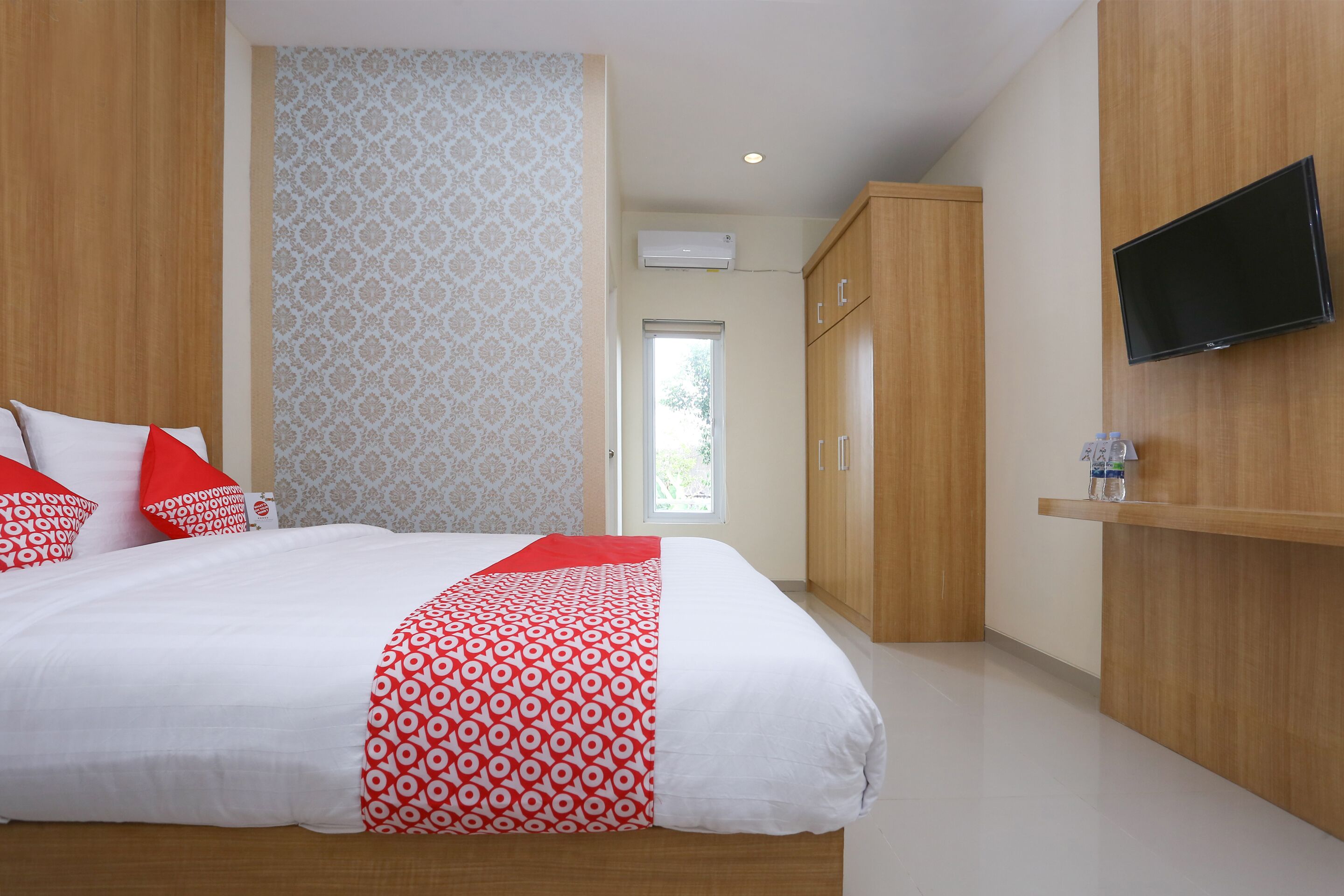 Quarto de hotel com cama grande, guarda-roupa de madeira e televisão presa na parede.