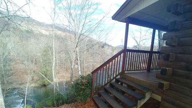 A wooden cabin with a porch overlooking a river and forested hills.