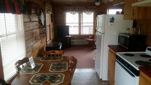 A wooden cabin interior with a dining table, chairs, a refrigerator, a stove, and a television.