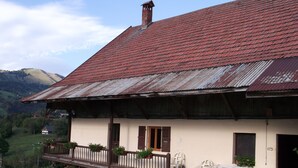 A rustic building with a red-tiled roof, wooden balcony, and outdoor seating area. - Renovated farmhouse with panoramic views  (Le Bouchet Mont Charvin)