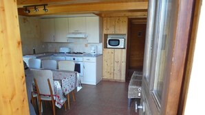 A compact kitchen with white cabinets, a microwave, and a dining area with a table and chairs. - Renovated farmhouse with panoramic views  (Le Bouchet Mont Charvin)