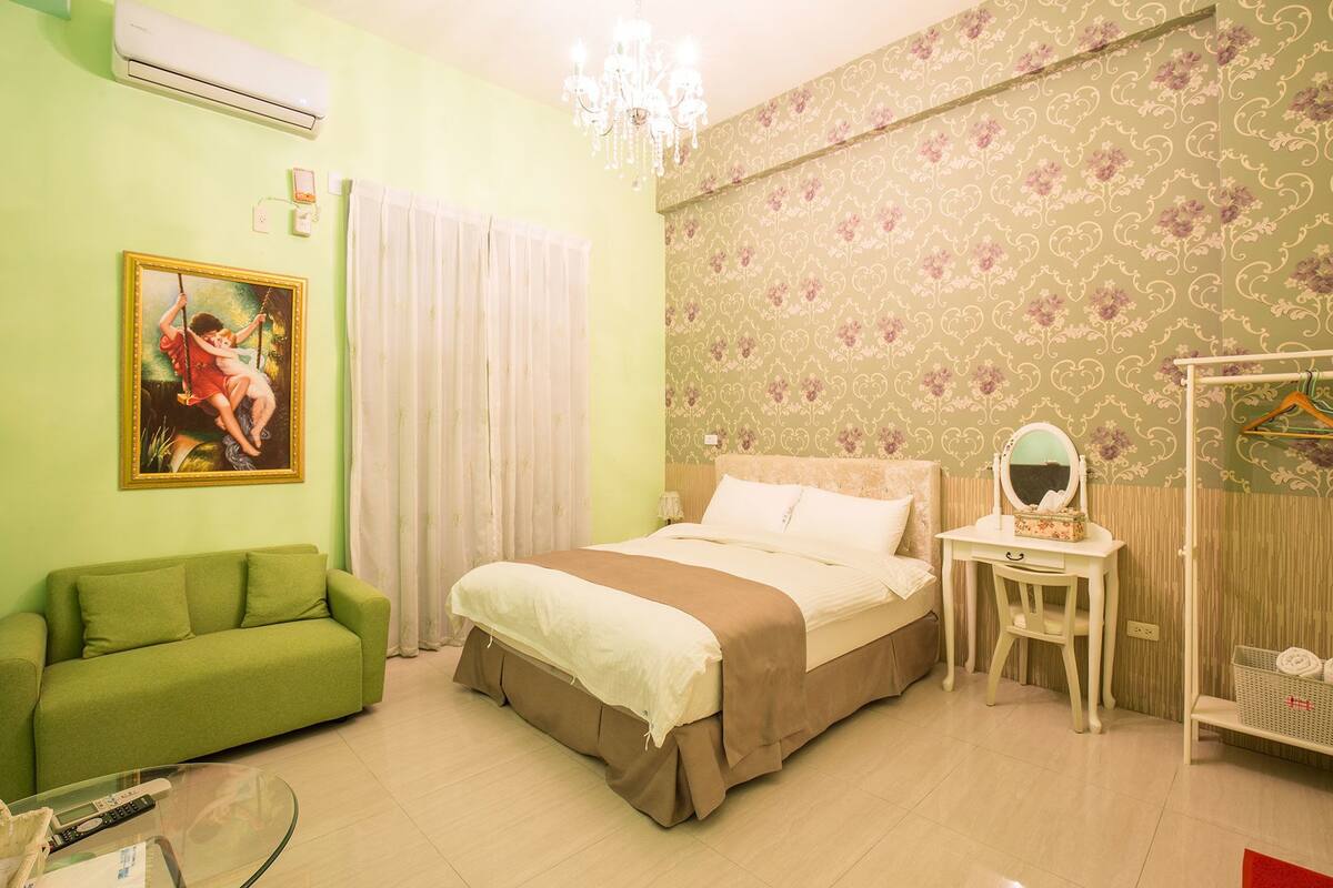 A room with a bed, a green sofa, a small table with a mirror, and a chandelier.