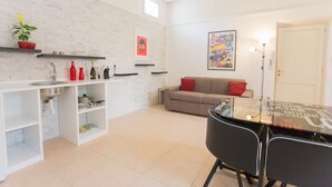 Eine moderne Küche mit weißen Ziegelwänden, einem Esstisch mit Stühlen, einer Couch und einer roten Pflanze.