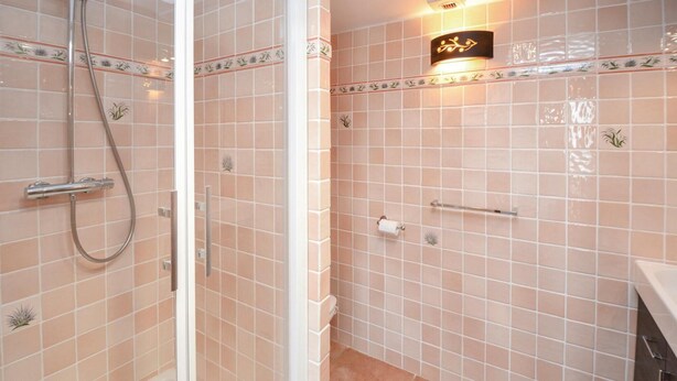 Une salle de bain avec des carreaux roses, une douche avec une porte en verre, un porte-serviettes et un luminaire fixé au mur.