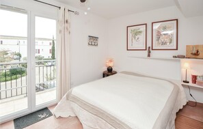 A bedroom with a large bed, a balcony with a view of buildings, a small table with a lamp, and wall art.