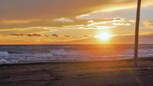 Une scène de plage au coucher du soleil sur l’océan, avec des vagues qui déferlent sur le rivage et un poteau au premier plan.