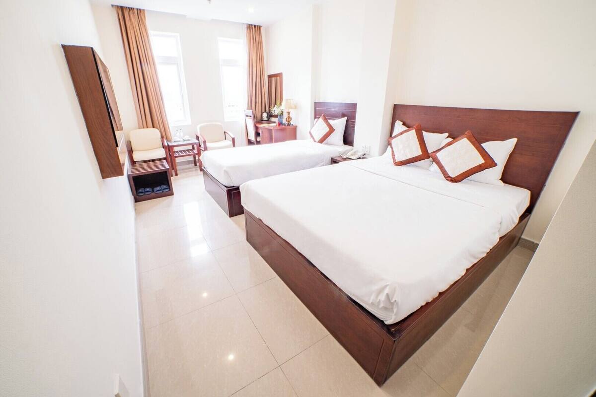 A hotel room with two beds, a desk, a chair, and a shoe rack.
