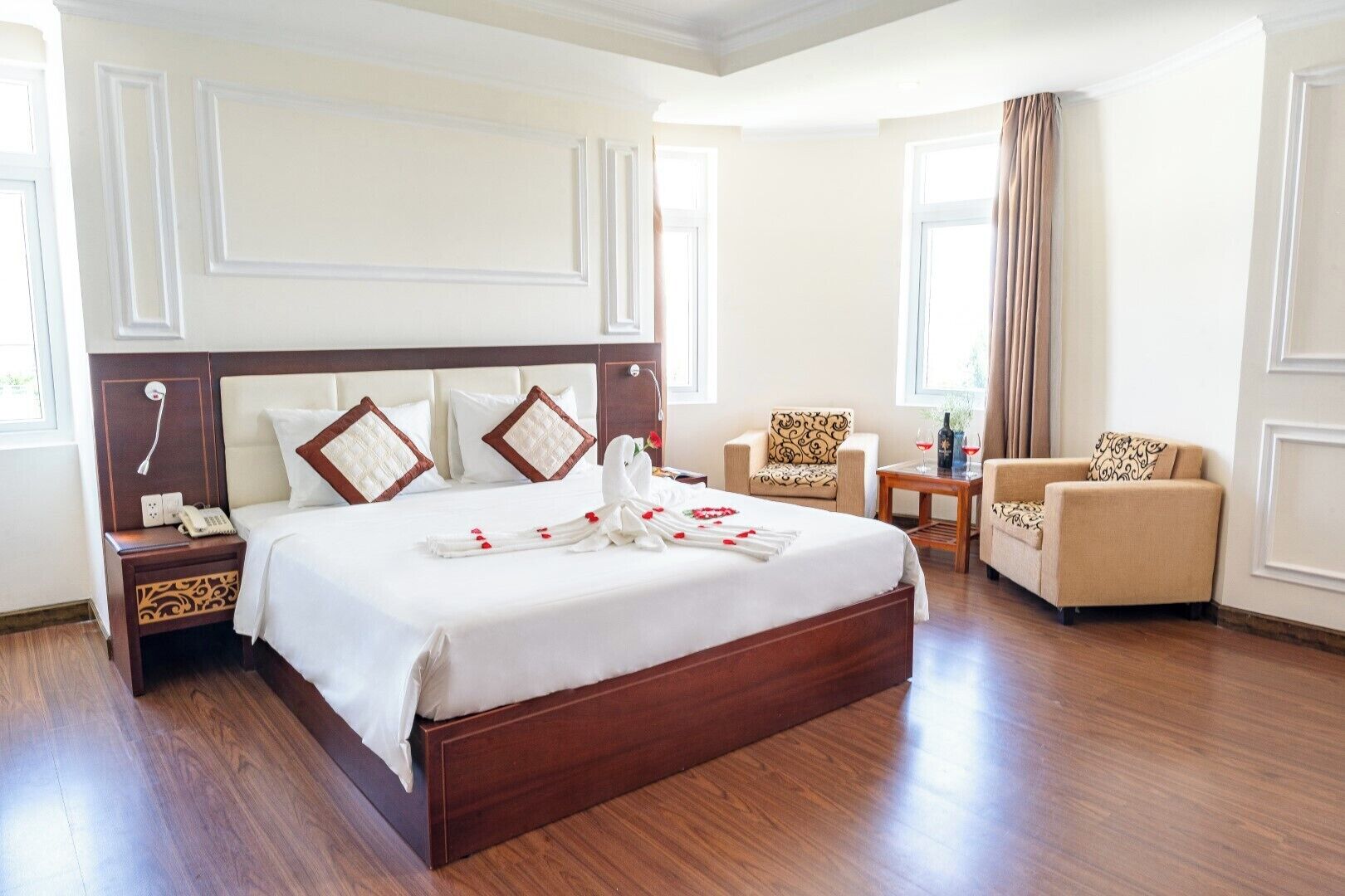 Een hotelkamer met een groot bed, twee fauteuils, een klein tafeltje en een nachtkastje.
