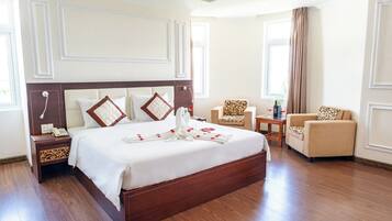 Een hotelkamer met een groot bed, twee fauteuils, een klein tafeltje en een nachtkastje.